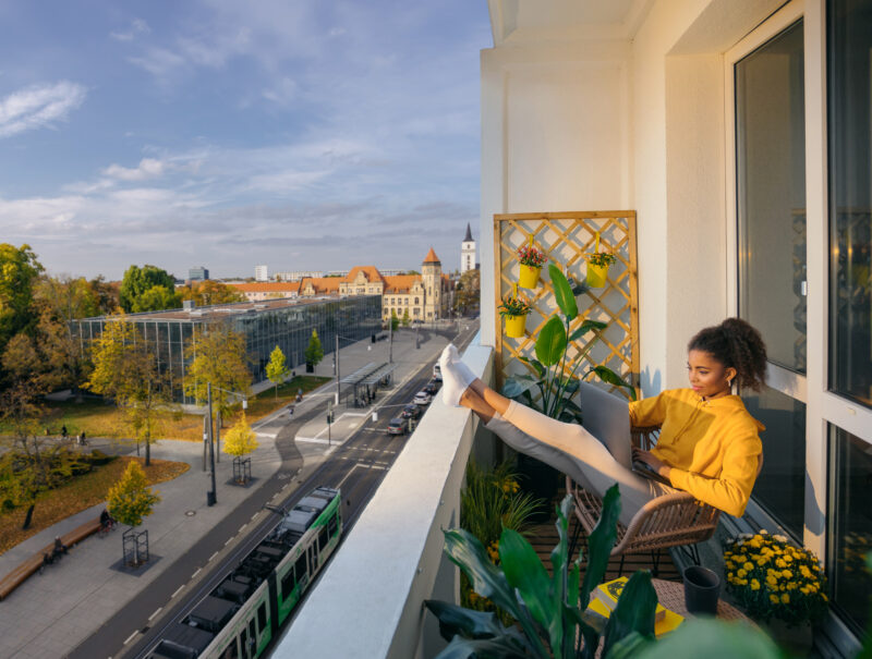Junge Frau sitzt arbeitend auf ihrem Balkon